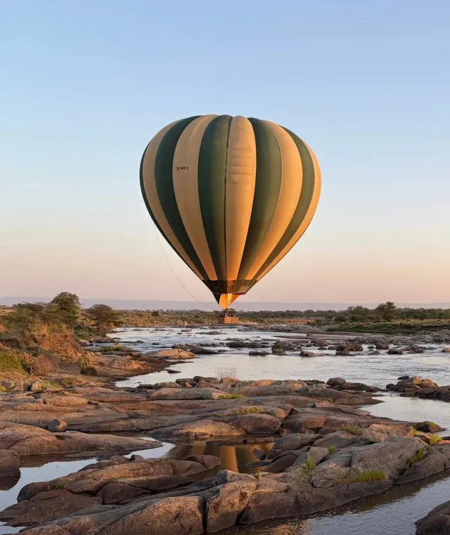 Mongolfiera in volo all’alba sopra un fiume del Serengeti